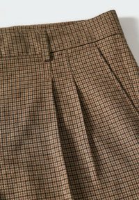 Ruskotaiset ruudulliset housut, joissa on teksturoitu pinta, pleateilla ja sileällä vyötärönauhalla. Kuvio koostuu pienistä ruudukoista tummissa ja vaaleissa sävyissä.