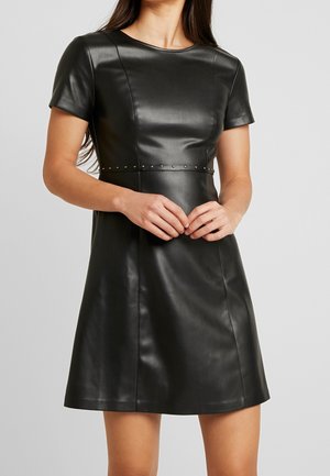 Černé šaty z umělé kůže s krátkými rukávy, přiléhavým živůtkem, rozšířenou sukní a kovovými cvoky zvýrazňujícími šev v pase. Hladká textura.