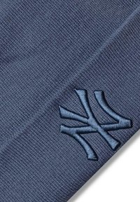 Tummansininen neulepipo, jossa on teksturoitu pinta ja edessä brodeerattu vaaleansininen logo, joka muistuttaa "N":tä ja "Y":tä.