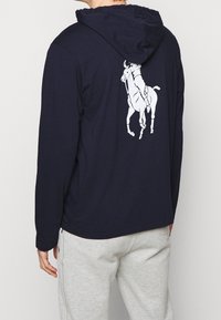 Námořnická mikina s kapucí, na zadní straně s velkým bílým grafickým motivem jezdec na koni, vyrobená z měkké látky, s dlouhými rukávy a uvolněným střihem.