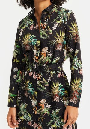 Sort langærmet kjole med knapper foran med tropisk blomstermønster, der indeholder grønne, orange og hvide blomster samt et matchende bælte med rund spænde.