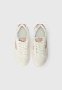 Hvide sneakers med beige detaljer og et tekstureret glitrende sidepanel. De har flade snørebånd og en polstret tunge for komfort.