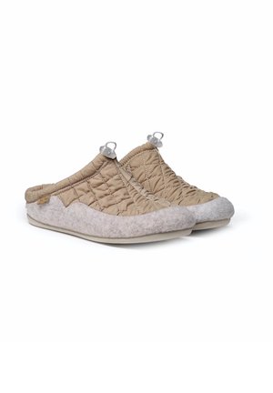 Beige doorgestikte instapslippers met lichtgrijze vilten rand en verstelbare koordsluitingen op een platte zool, schuin bekeken.