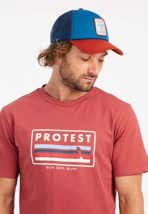 Rode katoenen T-shirt met "PROTEST" logo en golfafbeelding, gecombineerd met een blauw en rood mesh pet met een rechthoekig patchlogo.