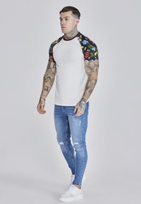 White fitted t-shirt with colorful floral pattern on sleeves, paired with light blue ripped skinny jeans and white sneakers.