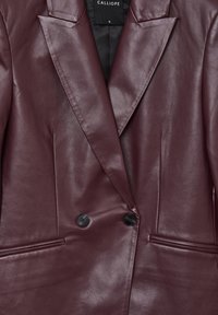 Blazer in ecopelle bordeaux scuro con rever larghi, due bottoni neri e tasche a fessura orizzontali sul davanti.