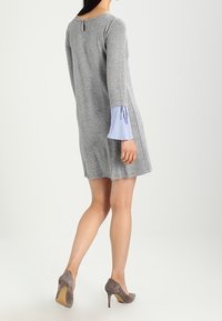 Grå stickad klänning med långa ärmar som har blå och vita randiga detaljer vid ärmsluten. Nyckelhålsdetalj på baksidan. Bärs med grå klackskor.