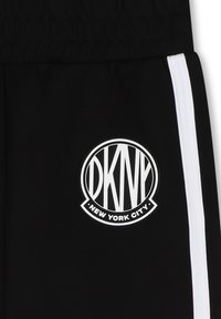 Pantalons de sport noirs avec des rayures blanches sur les côtés. Présente un logo circulaire DKNY avec le texte "NEW YORK CITY" sur un tissu texturé.