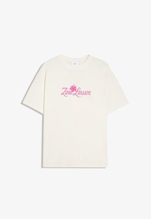 Wit T-shirt met korte mouwen met roze tekst "Zara Larsson" en hibiscusbloemgrafiek in het midden van de borst.