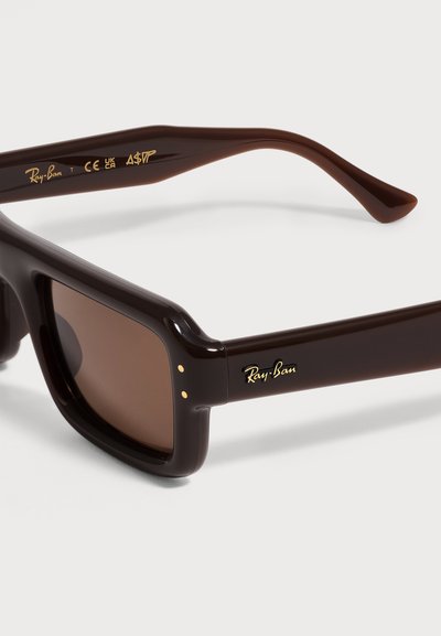 Тъмнокафяви слънчеви очила Ray-Ban с правоъгълни рамки, със златно лого на крачето и сертификатни маркировки от вътрешната страна на дръжката.