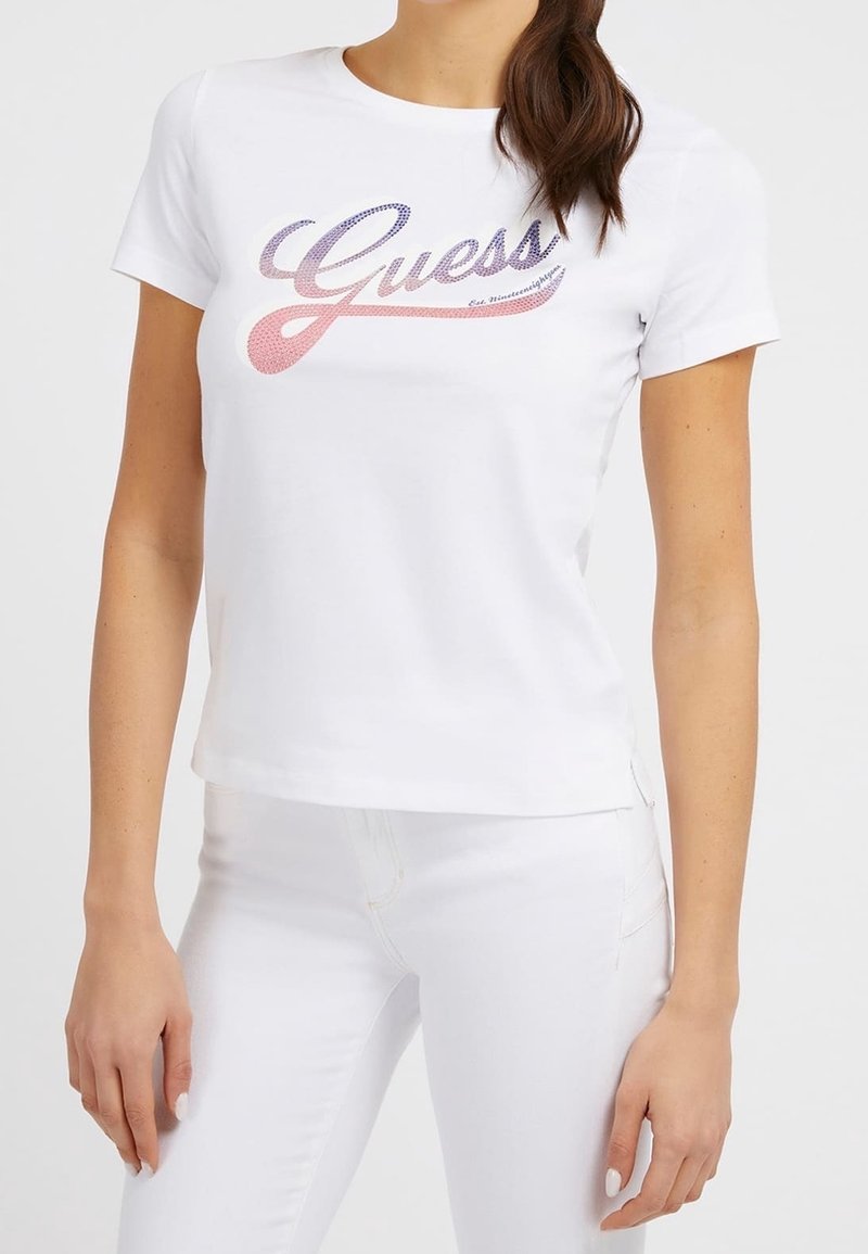 T-shirt en coton blanc à manches courtes, avec un logo "Guess" coloré en rose et bleu sur le devant. Coupe ajustée.