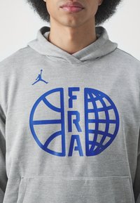 Felpa grigia con tasca a marsupio frontale, con grafica blu di un pallone da basket e la scritta "FRA" in lettere in grassetto. Include il logo Jumpman.