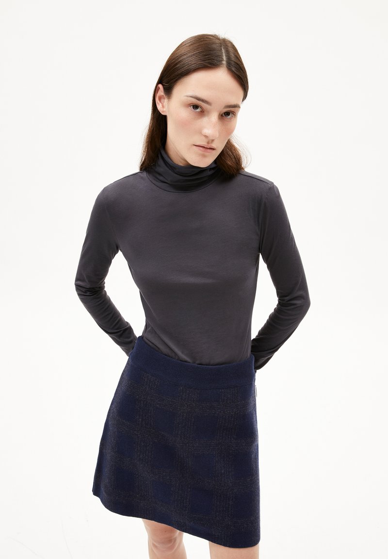 Langärmliges, eng anliegendes Rollkragenoberteil aus dunkelgrauem Stoff, kombiniert mit einem marineblauen Minirock mit einem strukturierten Karomuster.