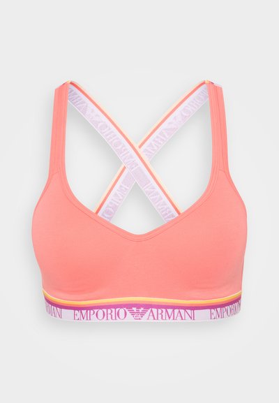 Coral sports bra with a V-neck, crisscross straps in white with purple text, and a band featuring a yellow accent and branded logo.