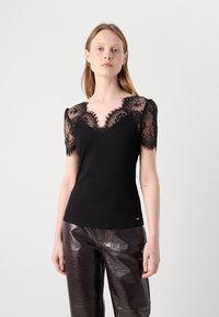 Haut noir avec des manches courtes en dentelle, décolleté en V, texture côtelée et corps lisse. Associé à un pantalon large brillant marron foncé.
