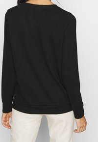 Svart långärmad tröja med rund halsringning. Mjuk textur och avslappnad passform, med ribbad nederkant och manschetter.