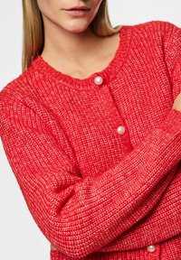 Röd stickad cardigan med rund halsringning och pärlknappar, med en texturerad väv och ribbade ärmslut för extra detaljer.