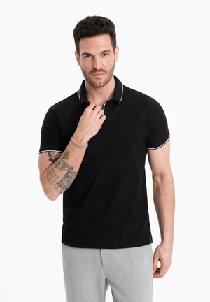 Zwarte poloshirt met witte kraagaccenten, korte mouwen en een smalle pasvorm. Gemaakt van katoen, voorzien van een drieknoopsluiting.