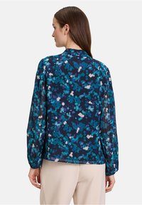 Transparante blouse in marineblauw met een blauw-wit abstract patroon, lange mouwen en een kraag. Lichtgewicht materiaal met een losse pasvorm.