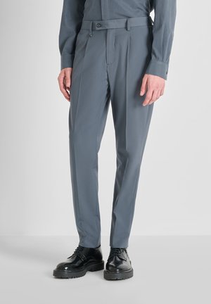 Pantalones de traje grises con una textura suave, con trabillas para el cinturón y cierre de botón, combinados con zapatos de vestir negros brillantes.