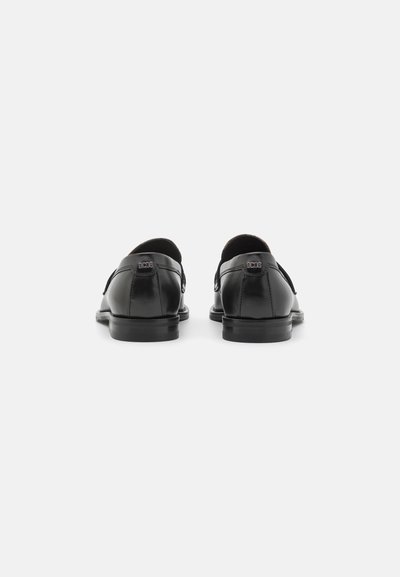 Chaussures en cuir noir au design élégant, avec un bout rond, un talon bas, une texture lisse, des coutures visibles et un détail de logo à l'arrière.
