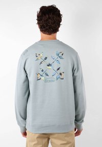 Sweatshirt bleu clair en coton, avec un motif de papillons colorés au dos, et des poignets et un ourlet côtelés.