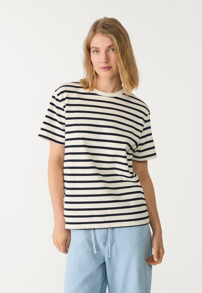 Stribet t-shirt i creme med marineblå striber, korte ærmer, rund halsudskæring og afslappet pasform, båret med lyseblå shorts med snoretræk.