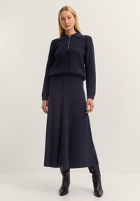 Marineblaues, geripptes Strickpullover- und Rock-Set. Mit einem Kragen und einem Reißverschluss sowie einer fließenden Silhouette. Kombiniert mit engen schwarzen Stiefeln.