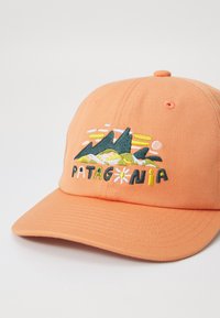 Casquette douce orange avec des motifs brodés de montagnes et de soleil. Texte "PATAGONIA" en noir et vert, avec des accents jaunes et blancs. En matière de coton.