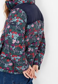 Blommig puffjacka med övre delen i mörk marinblått. Har ett livfullt blommönster, en figurnära silhuett och ribbade ärmslut.