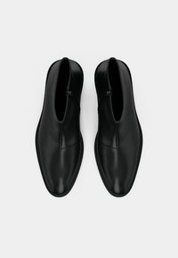 Melnas ādas potītes zābakus ar gludu apdari, ar rāvējslēdzēju un smailo purngalu. Plakana zole ar tonāliem šuvumiem.