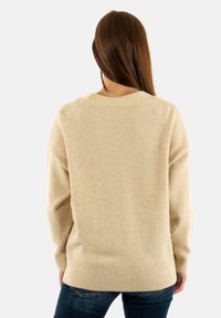 Maglione oversize beige in morbido tessuto testurizzato. Caratterizzato da un orlo e polsini a costine, con un ampio scollo a girocollo e maniche con cuciture abbassate.