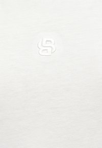 Tissu blanc avec un logo en relief subtil présentant les lettres entrelacées « B » et « S » au centre.