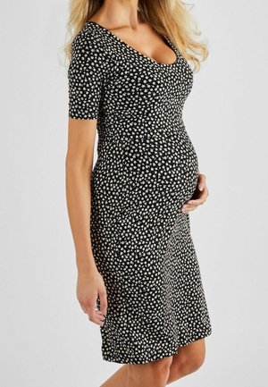 Schwarzes Maternity-Kleid mit kurzen Ärmeln, verziert mit einem weißen Blumenmuster, tailliertem Oberteil und einem schwingenden Rock, der das Wachstum des Bauches berücksichtigt.