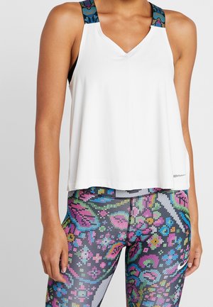 Person wearing white sleeveless top with patterned blue, pink, and green straps and vibrant multicolored floral leggings.