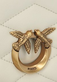 Borsa a tracolla in pelle bianca con un design trapuntato, accentuata da una hardware circolare in tono oro decorata con due figure di uccelli e logo impresso.
