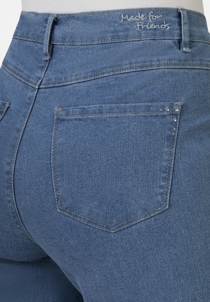 Blue denim high-waisted jeans feature a back view with two rear pockets, stitching details, and "Made for Friends" embroidered on the waistband.