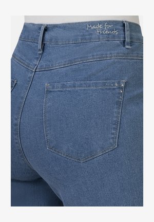 Blaue hochgeschnittene Jeans aus Denim zeigen eine Rückansicht mit zwei Gesäßtaschen, Nähdetails und dem Schriftzug "Made for Friends" auf dem Bund.