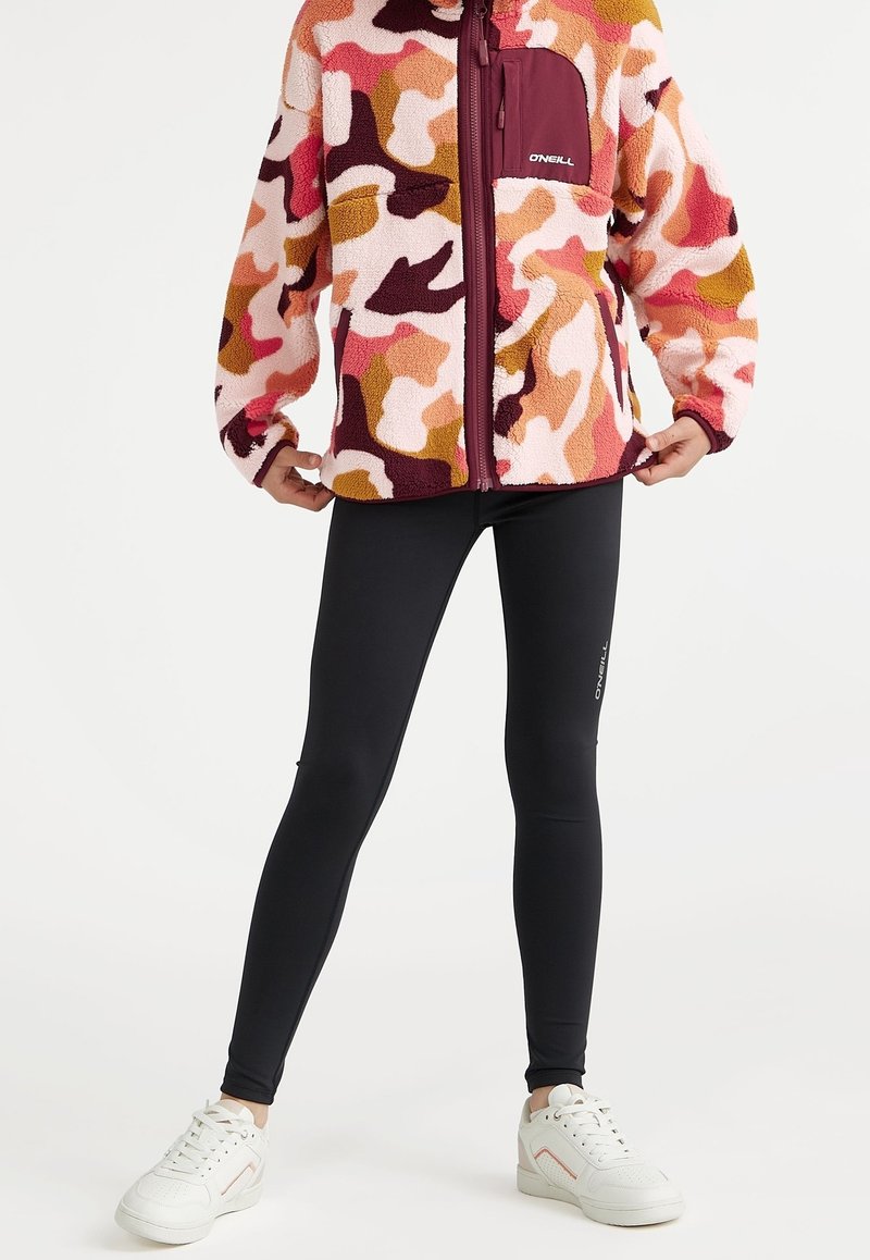 Veste polaire à motif camouflage multicolore avec une poche à fermeture éclair bordeaux ; associée à des leggings noirs et des baskets blanches.