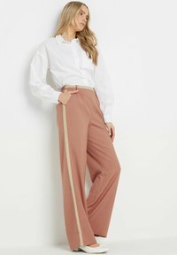 Lichtroze wijde broek met een beige zijkant, voorzien van een hoge taille en een zachte textuur, gecombineerd met een witte blouse met knopen.