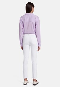 Chemise légère violette à boutons avec une coupe décontractée, associée à un jean blanc slim. La chemise présente un design simple à l'arrière.