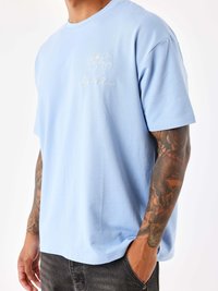 Camiseta de algodón azul claro con mangas cortas, que presenta un diseño de corazón bordado en blanco con un globo y el texto "Proyecto París".