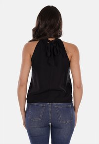 Top halter nero con chiusura a fiocco sul retro, caratterizzato da una texture liscia. Abbinato a jeans in denim blu aderenti.