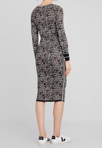 Robe ajustée à manches longues avec imprimé léopard, bandes latérales noires contrastantes et poignets côtelés. Portée avec des baskets blanches.