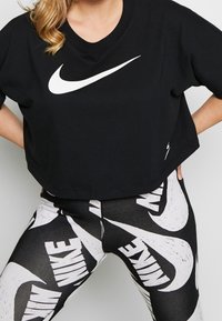 Svart kortärmad t-shirt med vitt Nike swoosh-logotyp på framsidan, tillsammans med högmidjade leggings som har ett djärvt svart och vitt Nike-mönster.