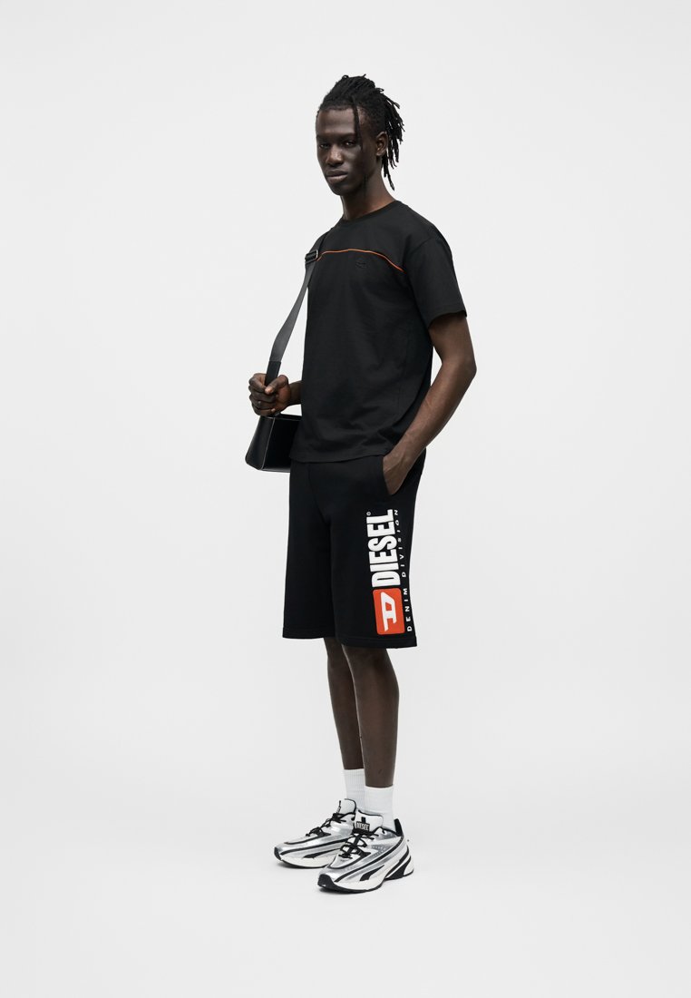 T-shirt noir à manches courtes avec un accent orange, associé à un short noir affichant le logo blanc "DIESEL". Complété par des chaussures de sport argentées.