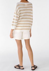 Beige en witte gestreepte gebreide trui met driekwartmouwen, gecombineerd met witte shorts en zwarte sandalen met kruisbandjes.