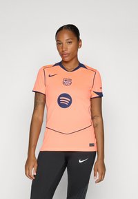 Oranje Nike-shirt met marineblauwe accenten, met een Barcelona-embleem en een circulair Spotify-logo. Korte mouwen en een V-hals ontwerp.