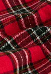 Tessuto a quadri rosso e nero con accenti bianchi e verdi. Texture morbida con un motivo intrecciato che presenta dimensioni quadrate variabili e linee prominenti.