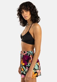 Haut de bikini noir avec fronces, associé à un short à imprimé floral coloré doté d'une taille à cordon. L'ensemble allie des couleurs et des motifs audacieux.